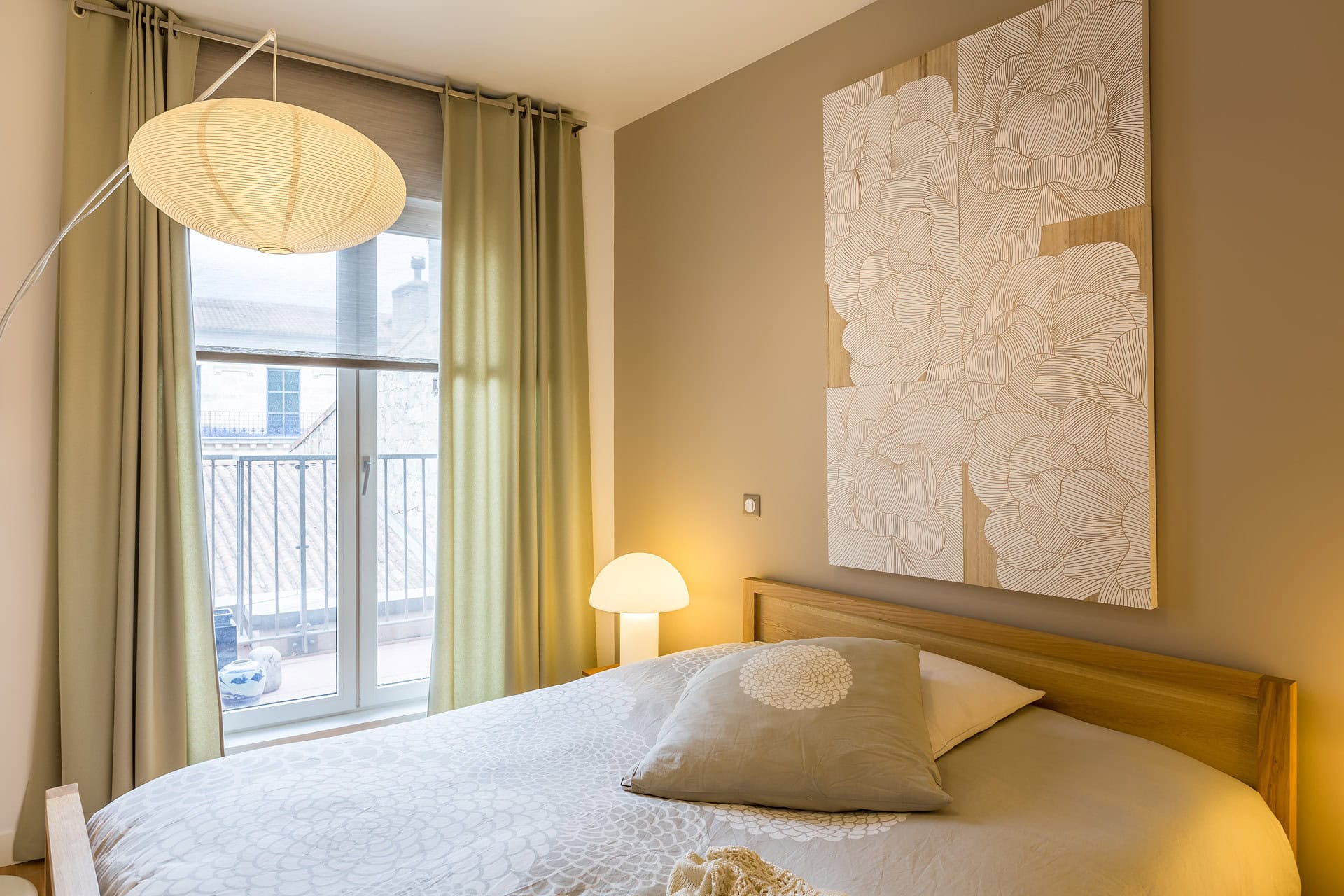 Chambre lumineuse avec lit en bois, luminaire suspendu et décoration florale murale