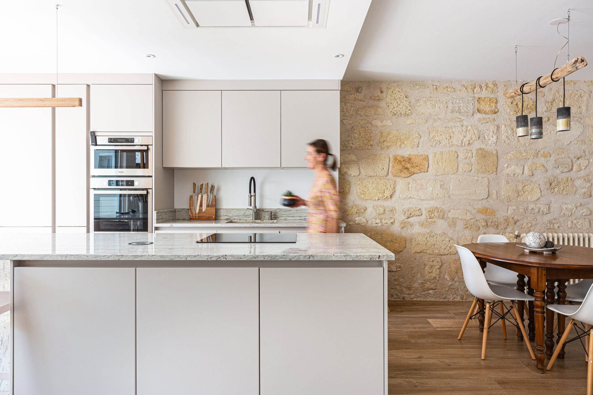 Cuisine avec îlot en marbre et mur en pierre donnant sur une salle à manger au design épuré.